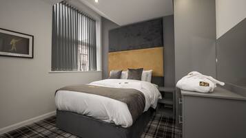 Una habitación de hotel moderna con una cama grande, un cabecero con diseño texturizado, una ventana con persianas, un cuadro en la pared y una bata colgada en un armario.