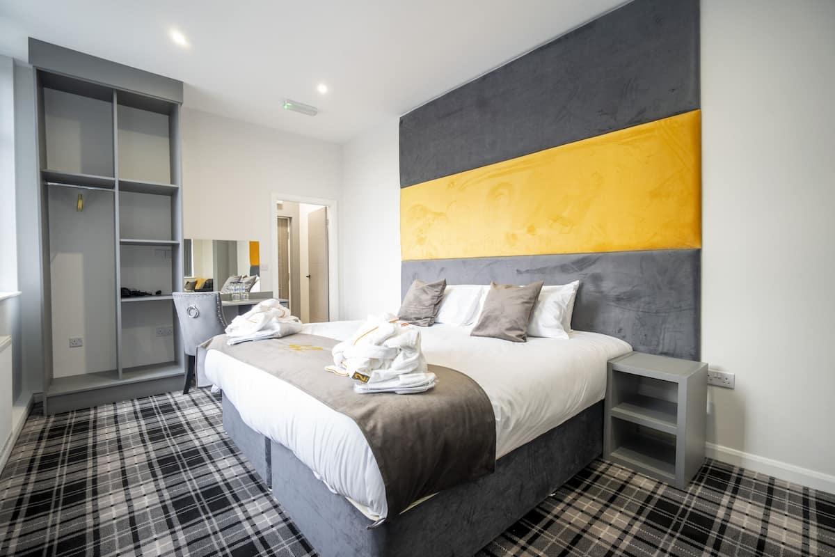 A modern hotel room with a large bed, grey wardrobe, and a unique wall art piece.