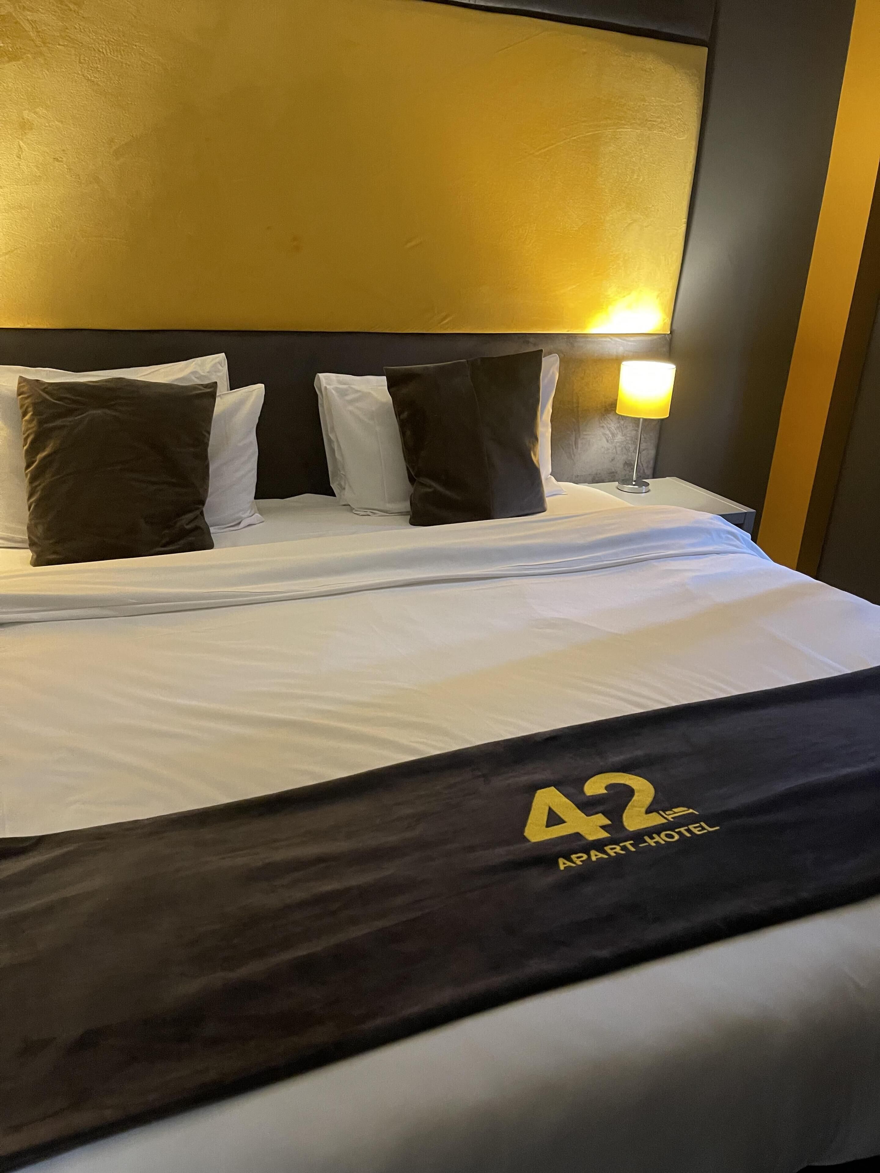 Ein Hotelzimmer mit einem Bett, Kissen, einem Kopfteil und einem Nachttisch mit einer Lampe.
