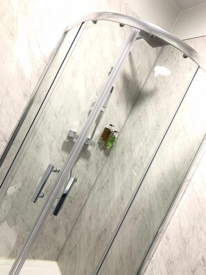 A glass-enclosed shower with a chrome frame, a handheld showerhead, and a soap dispenser. - 42 Apart-hotel (Scunthorpe)