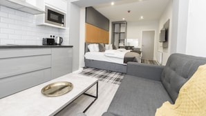 A modern hotel room with a kitchenette, a bed with a headboard, a gray sofa, and a small table. - 42 Apart-hotel (Scunthorpe)
