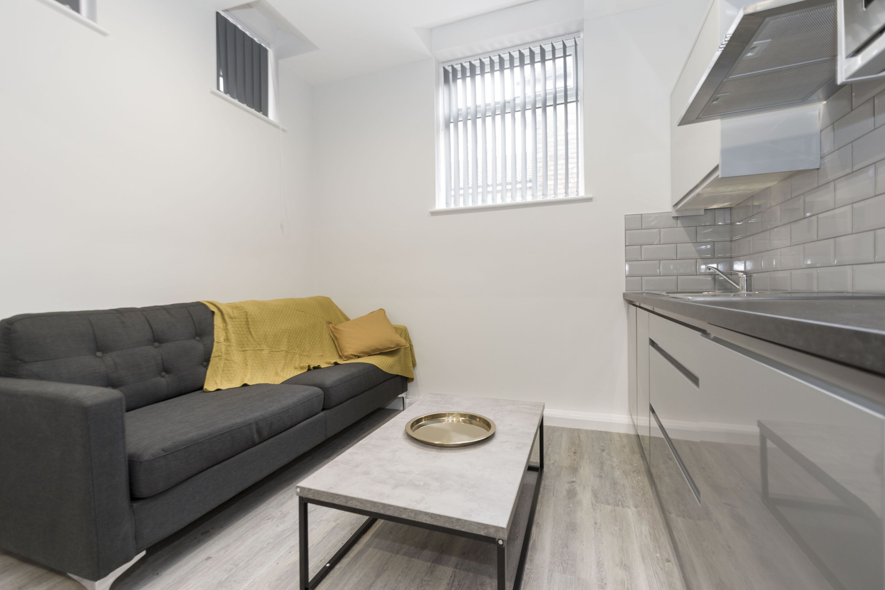 A compact kitchen with a grey sofa, a small table, and a window with blinds.