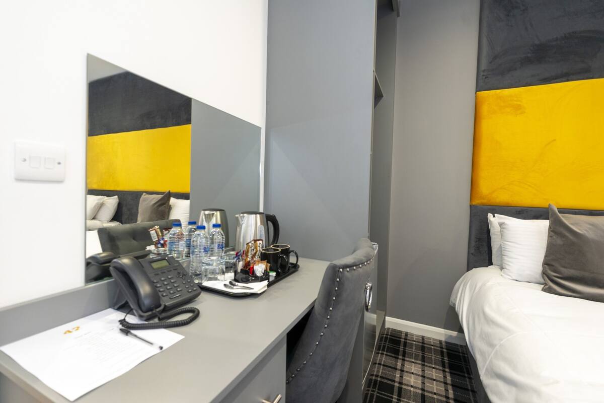 A hotel room with a desk, a telephone, a coffee maker, and a bed with pillows.