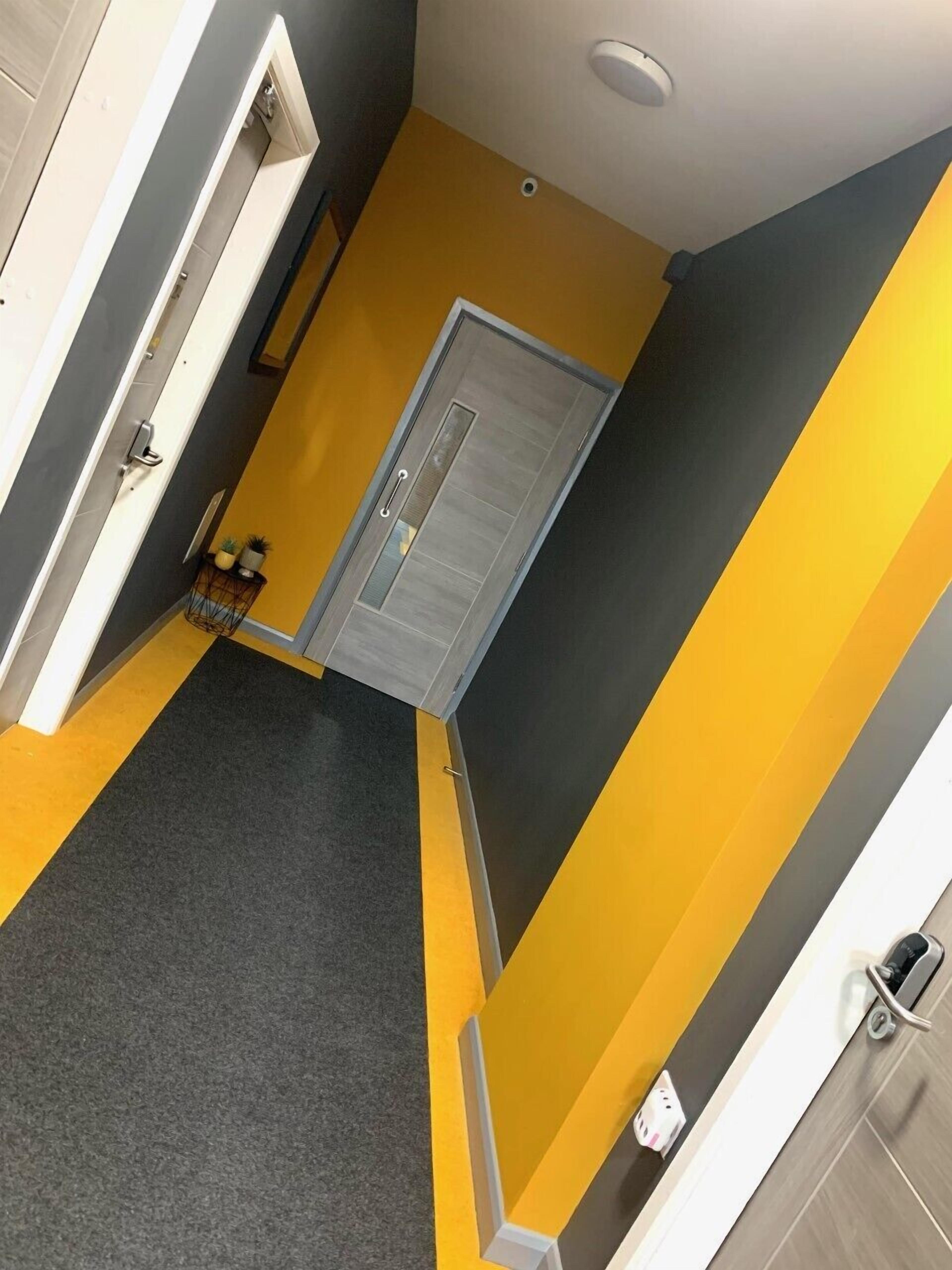 Un pasillo con una puerta gris, paredes amarillas y una alfombra gris.