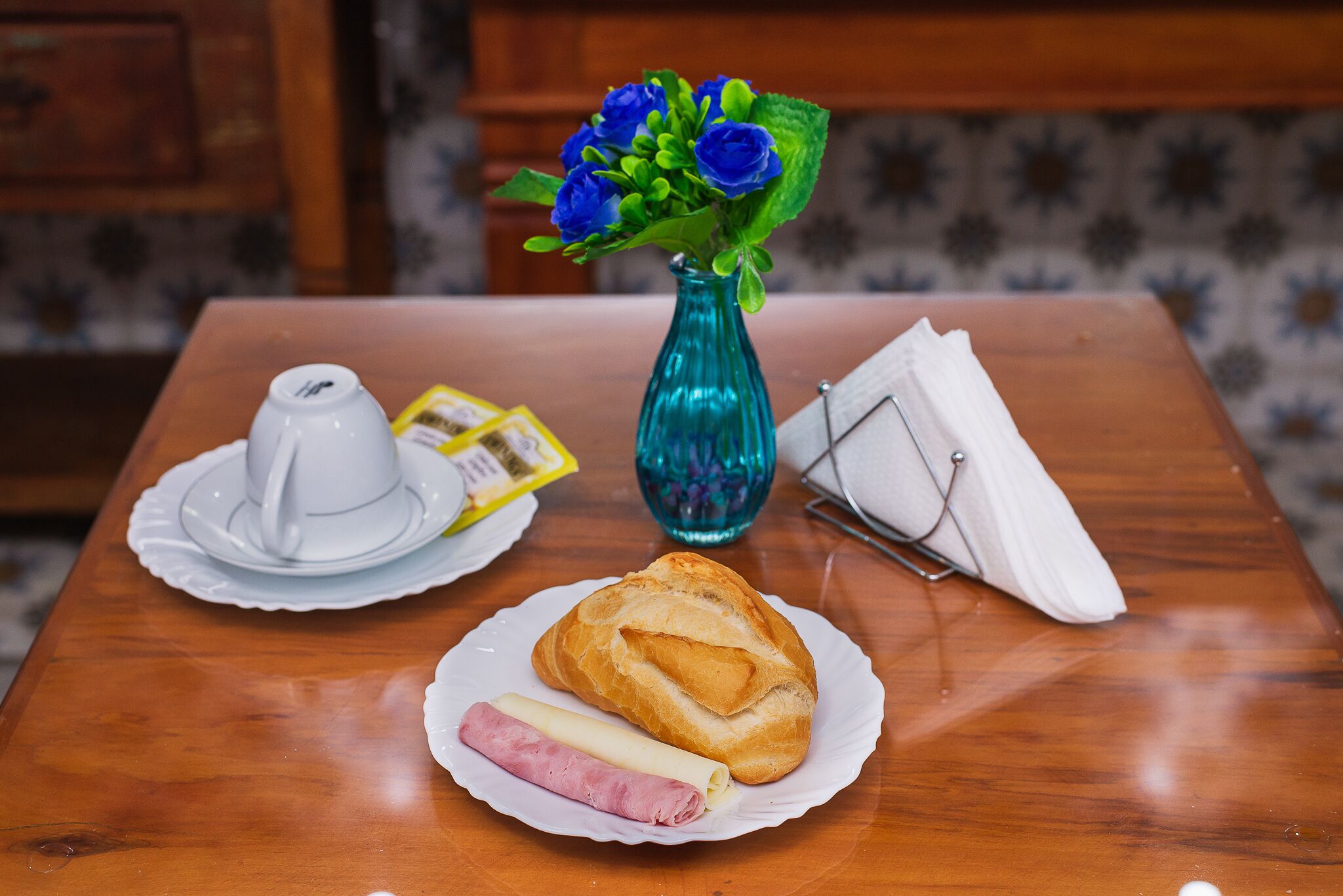 A wooden table with a plate of food, a blue vase with flowers, and a white teapot.
