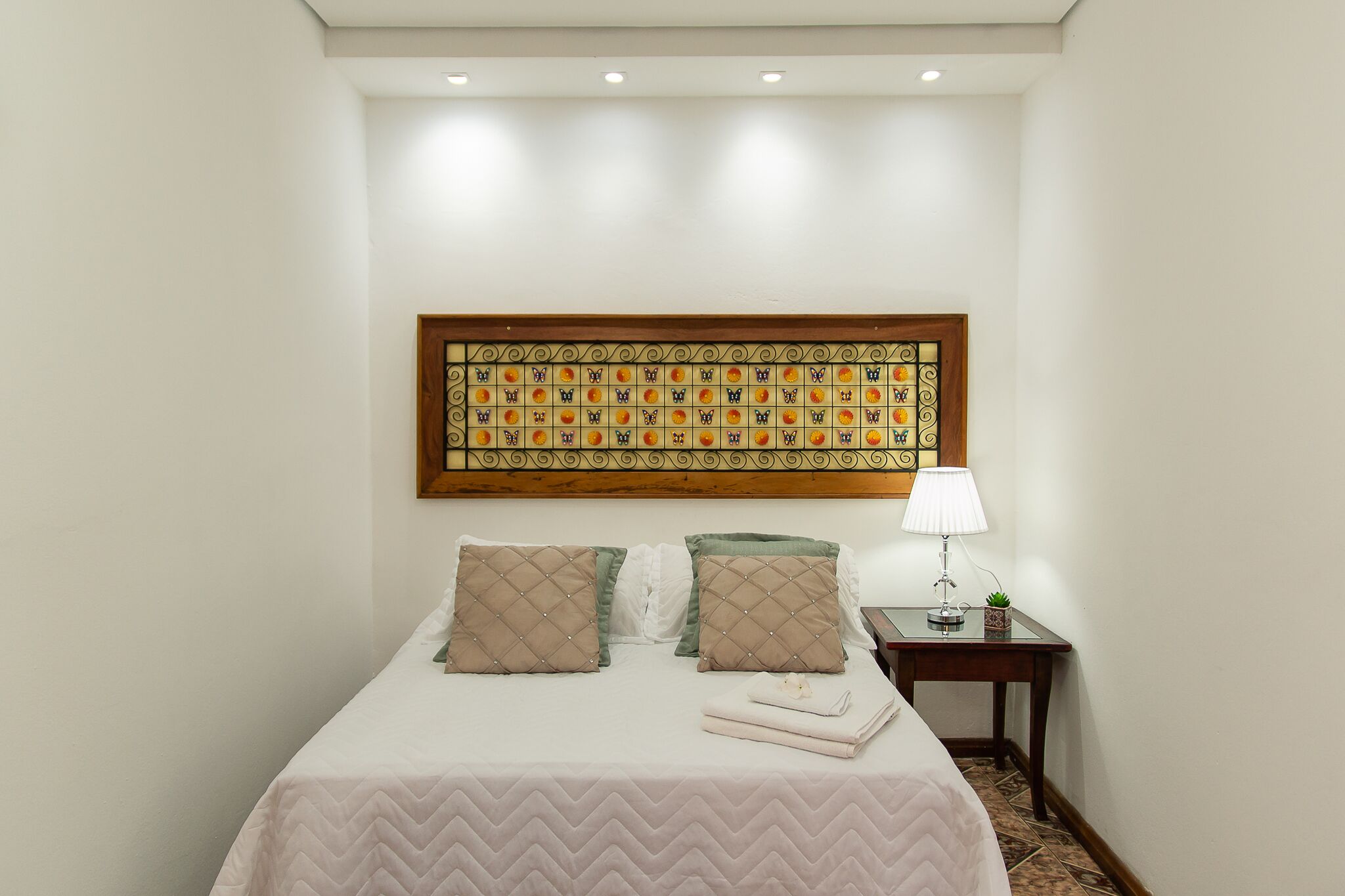 A hotel room with a bed, a nightstand with a lamp, and a decorative wall piece.