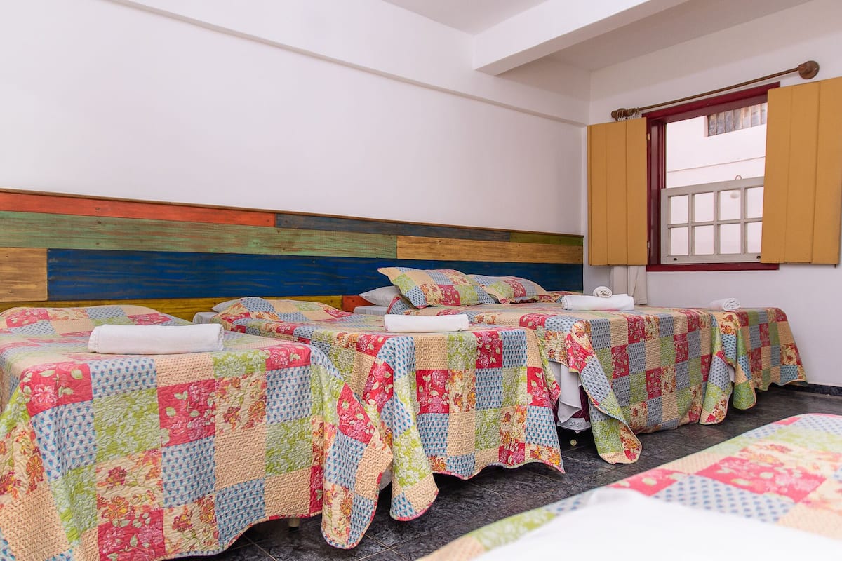 Quarto de hotel com três camas, cada uma com um edredom colorido.