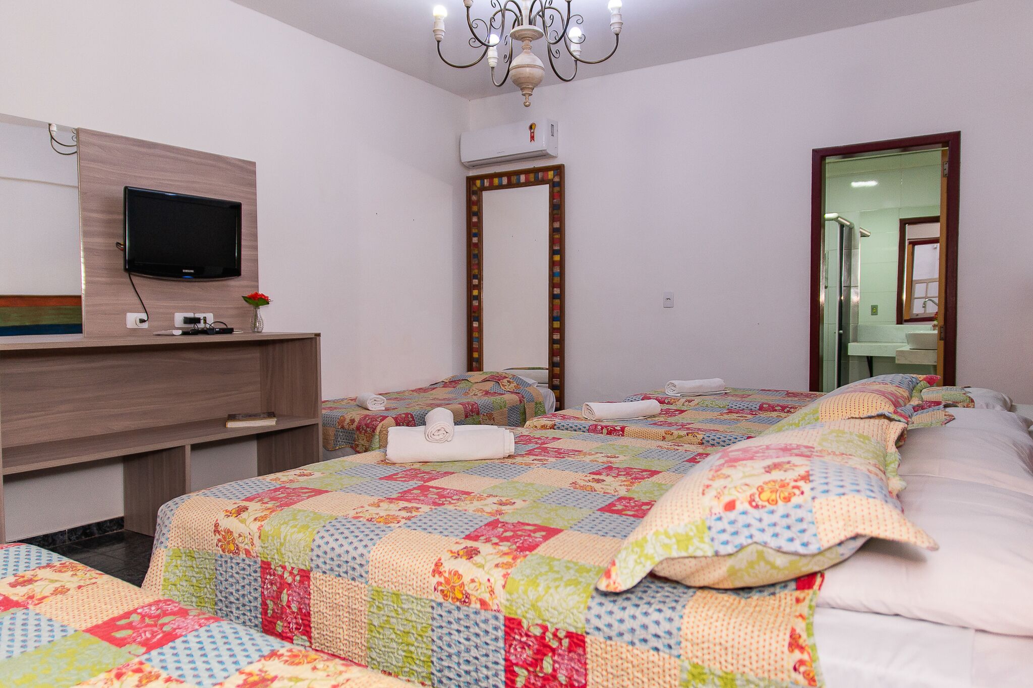 Habitación de hotel con televisión, espejo, escritorio con un jarrón y dos camas con colchas de colores.