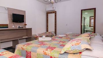 Habitación de hotel con televisión, espejo, escritorio con un jarrón y dos camas con colchas de colores.