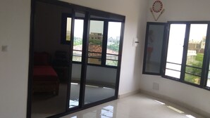 Una habitación amplia con un gran ventanal corredera que da a un balcón, un sofá rojo y una planta colgante.