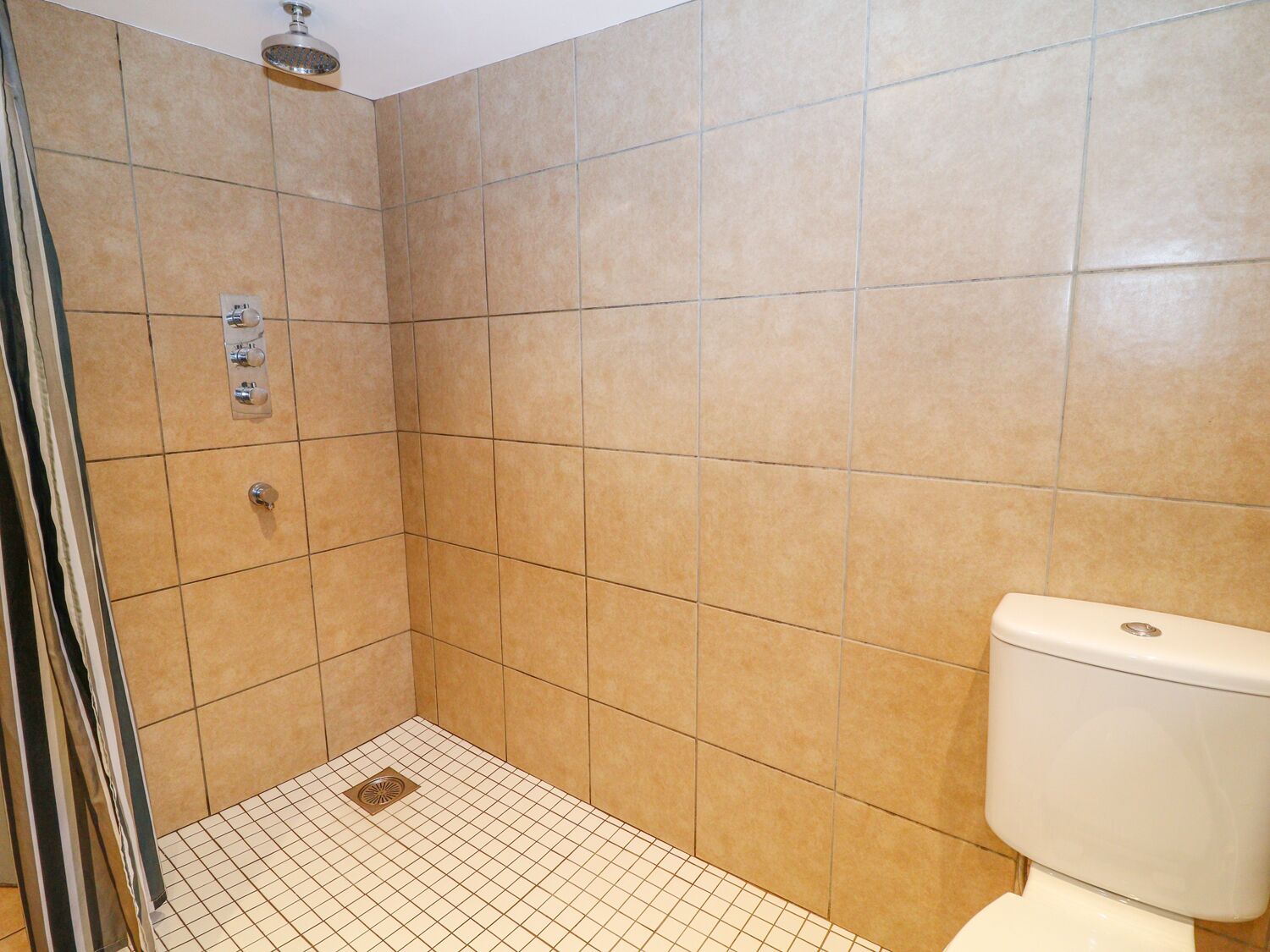 A small, tiled bathroom with a shower, a toilet, and a control panel for the shower.