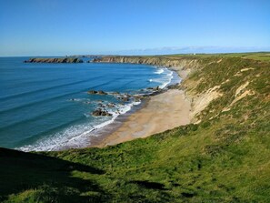 Un paysage côtier avec une plage de sable, des falaises herbeuses et une mer bleue et limpide.