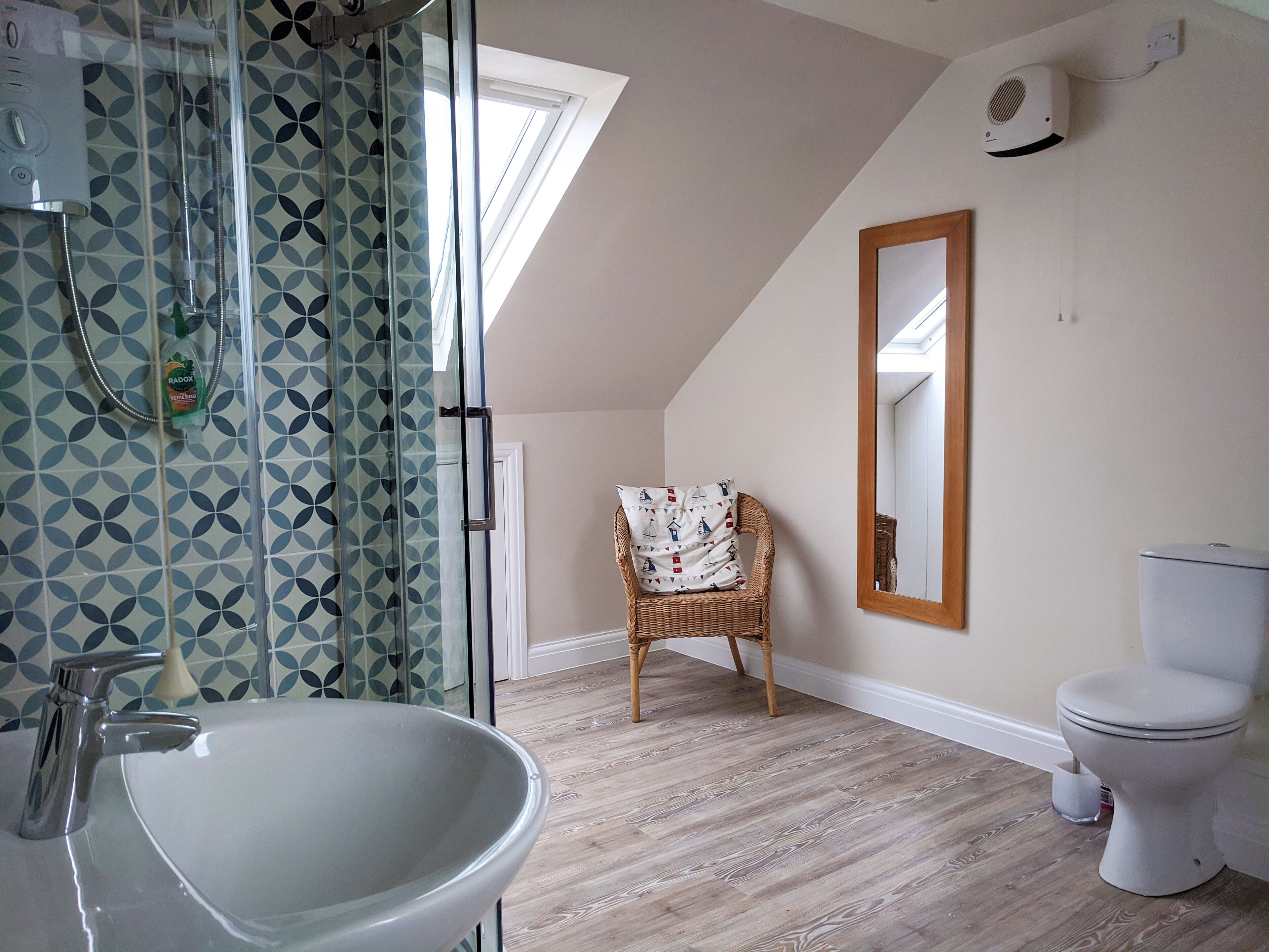 Un baño con cabina de ducha de vidrio, un lavabo blanco, un inodoro y una silla de mimbre.