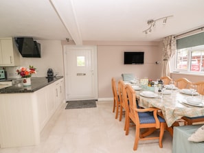 A compact kitchen with white cabinets, a black countertop, and a dining area with wooden chairs and a checkered tablecloth. - Fisher Granary (Lampeter)