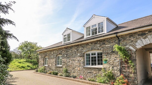 A stone building with a paved driveway and a small garden area with flowers and shrubs. - Fisher Granary (Lampeter)