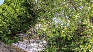 An outdoor patio with a table and chairs, surrounded by dense greenery and trees. - Fisher Granary (Lampeter)