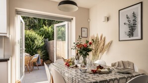 Un comedor con una mesa dispuesta para dos, un florero con flores y una planta enmarcada en la pared.