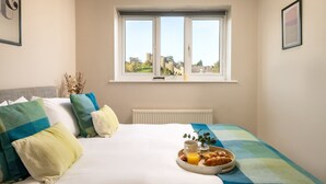 Un dormitorio con una cama, un ventanal con vistas a un castillo y una bandeja con cruasanes y jugo de naranja.