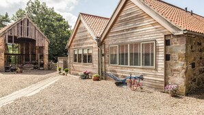 Un bâtiment rustique en bois, doté d’un toit en tuiles, d’un mur en pierre et d’une allée gravillonnée.