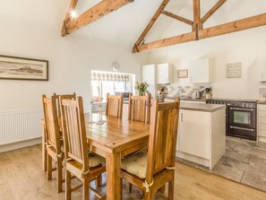 A cozy kitchen with wooden beams, a dining table with chairs, and a small island with a sink and stove. - Sawmill Cottage (Belford)