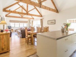 A spacious living area with a wooden dining table, chairs, and a kitchen island. - Sawmill Cottage (Belford)