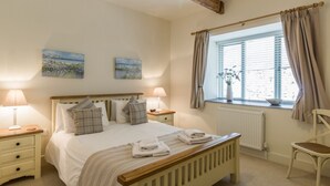 Une chambre à coucher avec un lit, deux tables de chevet, une fenêtre avec des rideaux et un radiateur.