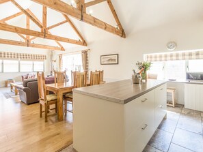 A spacious living area with a wooden dining table, chairs, a sofa, and a kitchen with a tiled backsplash and a clock on the wall. - Sawmill Cottage (Belford)