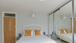 A bedroom with a bed, a wooden door, a nightstand, a lamp, and a large mirror. - Sandsfoot Rest (Weymouth)