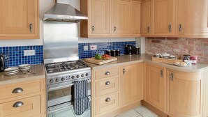 A modern kitchen with wooden cabinets, a stainless steel stove, and a blue-tiled backsplash. - Sandsfoot Rest (Weymouth)