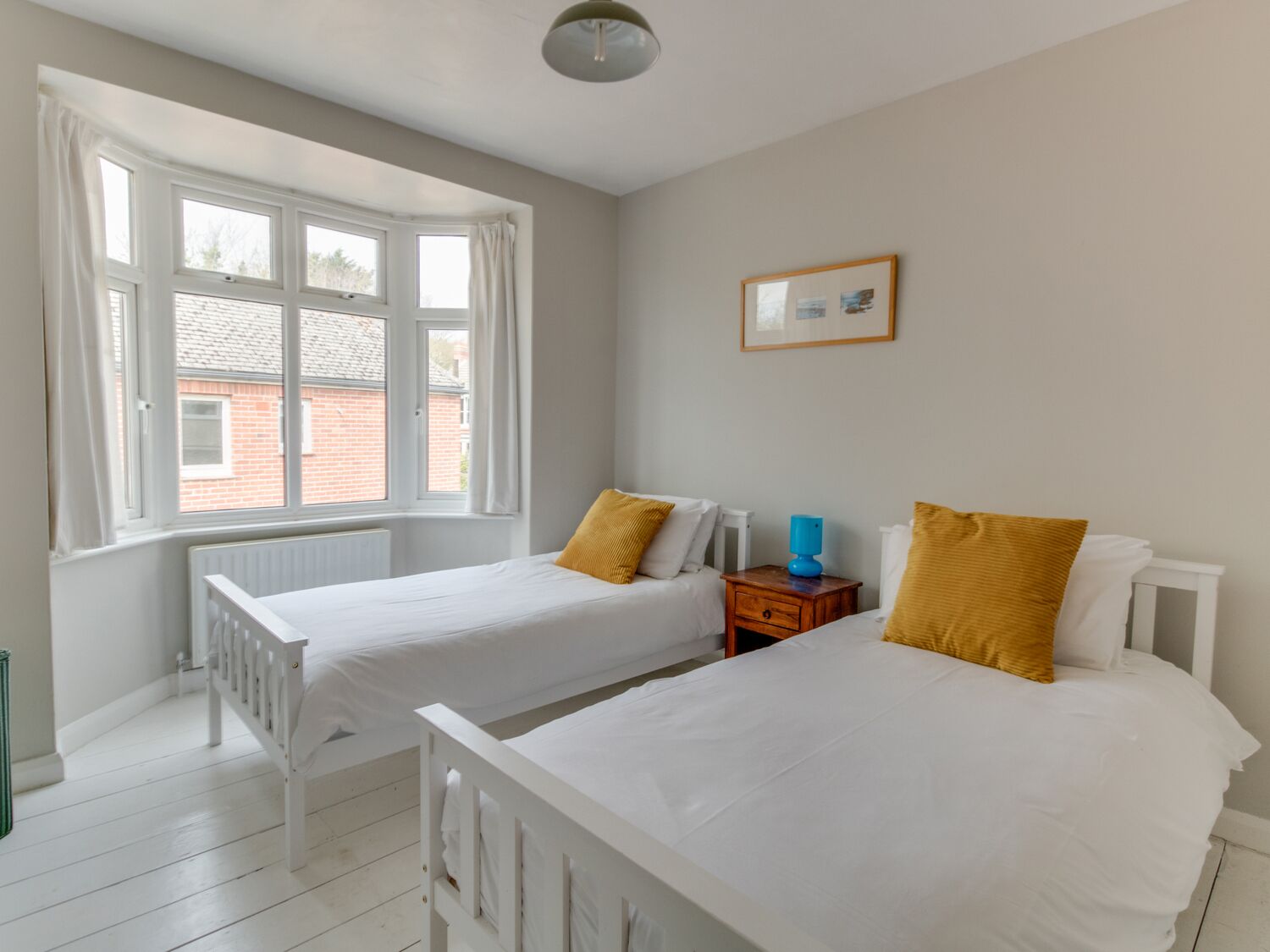 Een slaapkamer met twee bedden, een raam, een radiator en een ingelijst schilderij aan de muur.