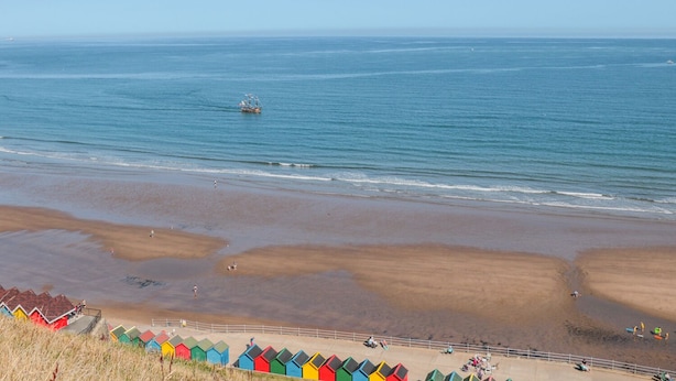 Une plage avec des cabanes colorées et un bateau sur l’eau.