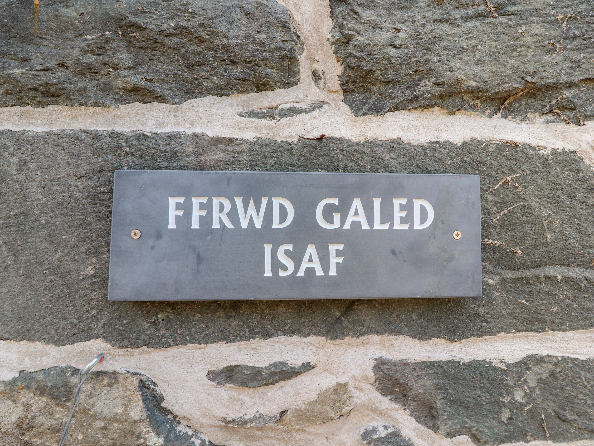 Une plaque de pierre portant l’inscription « FFRWD GALED ISAF » est fixée à un mur de pierre.