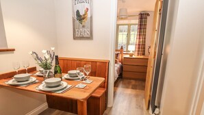 Un coin repas avec une table en bois dressée pour deux personnes, une bouteille de Bena Cucinà et un panneau mural indiquant « OEUFS FRAIS ».
