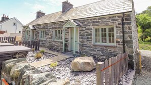 Une maison en pierre avec un toit à pignon, une clôture en bois et un chemin en pierre.