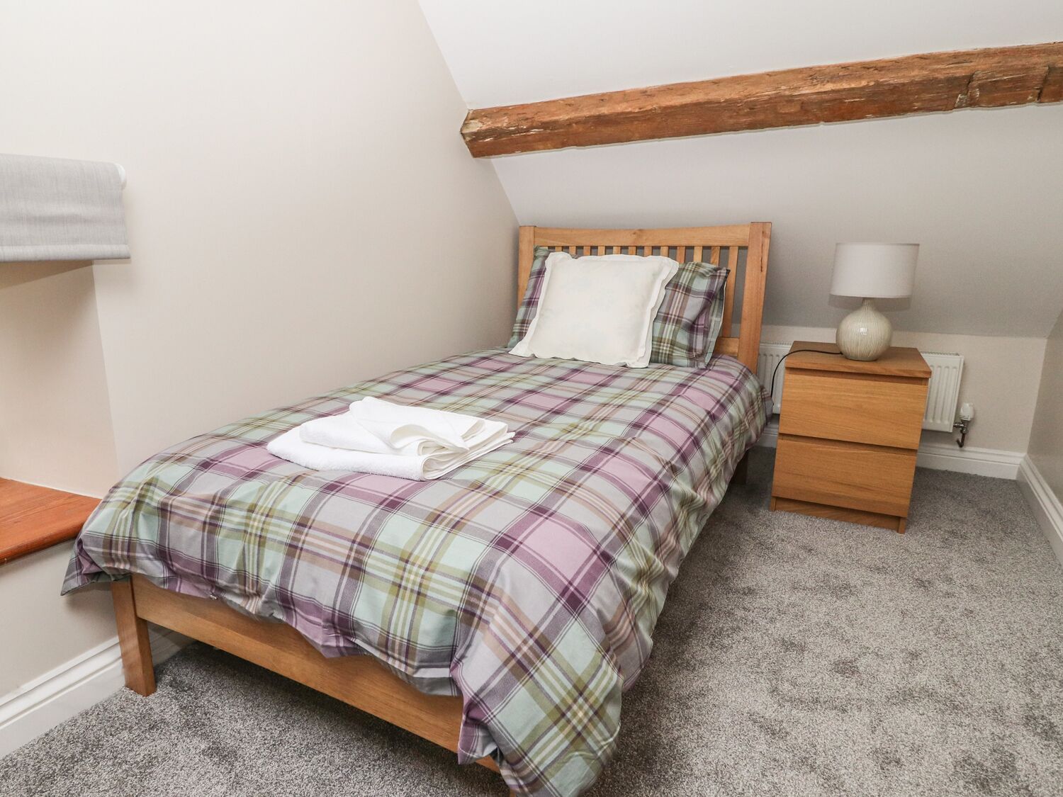 A bedroom with a wooden bed, plaid bedding, a nightstand with a lamp, and a radiator.