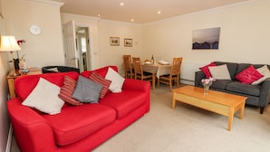 A living room with a red sofa, a grey sofa, a wooden coffee table, and a dining area with a table set for four. - Hurst View (Freshwater)