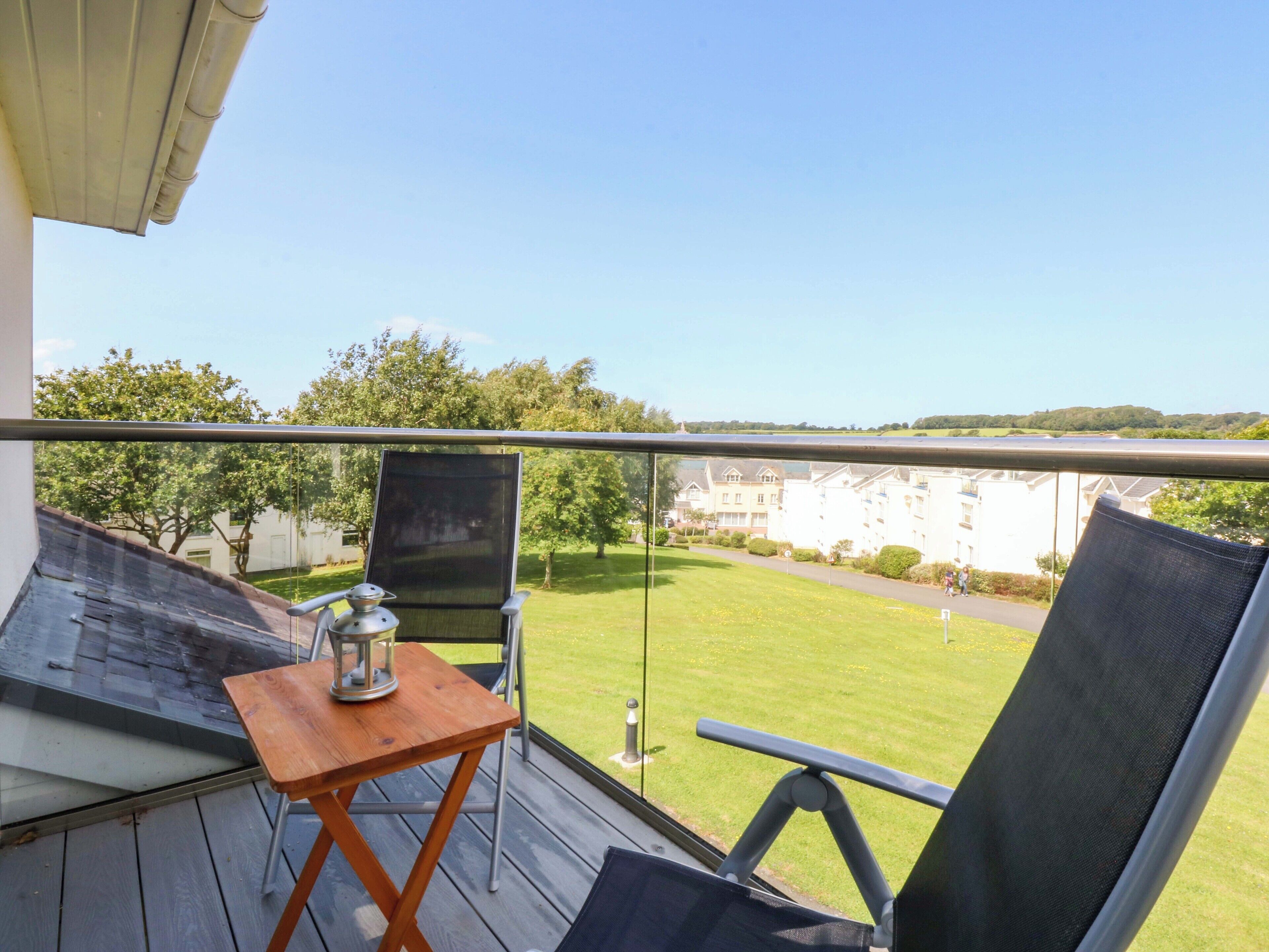 A balcony with a table, chairs, and a view of a green lawn and buildings.