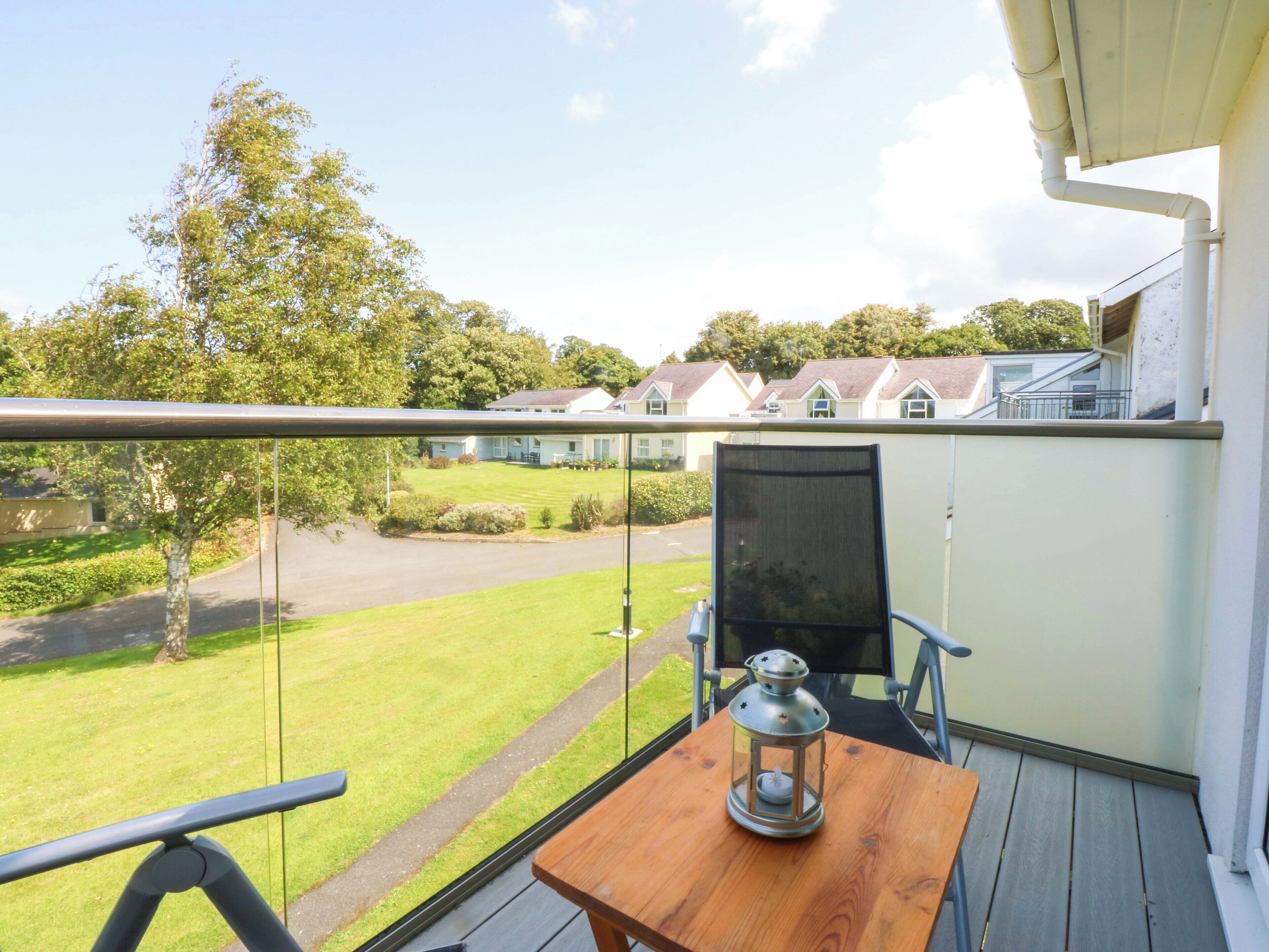 A balcony with a wooden table and a lantern, overlooking a well-maintained lawn and houses.