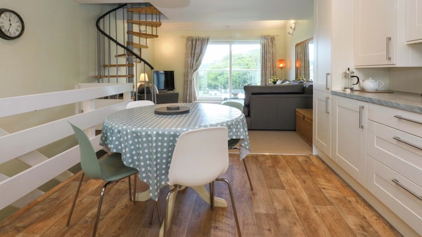 A dining area with a round table, chairs, and a polka dot tablecloth. There is a staircase leading to an upper level, a television, and a sofa in the background. - Machlud Ynys (Y Felinheli)