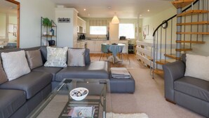 A modern living room with a glass coffee table, grey sofas, and a staircase. - Machlud Ynys (Y Felinheli)
