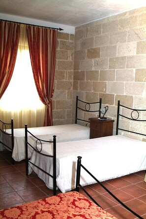 A room with two metal-framed beds, a brick wall, and a window with curtains. - Tenuta Santrifone (Secli)