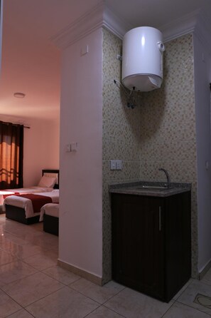 Une chambre d’hôtel comprenant un lit, une petite kitchenette avec un évier et un chauffe-eau fixé au mur.