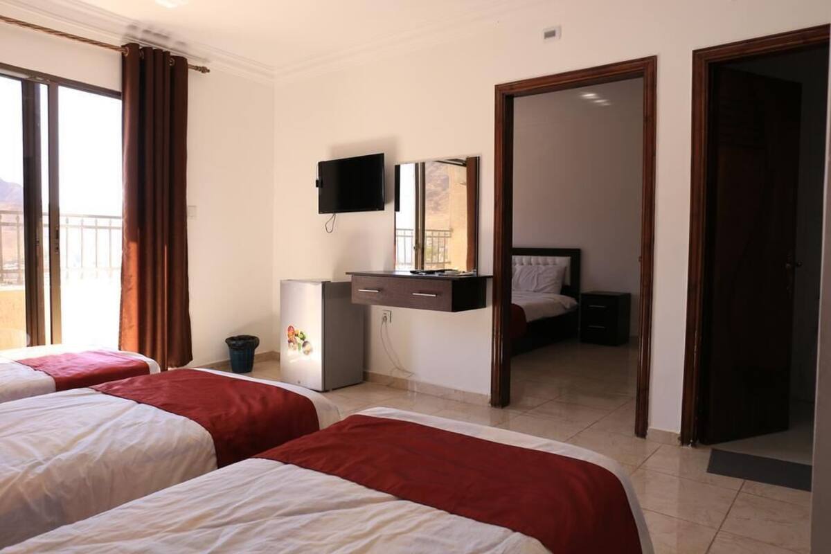A hotel room with two beds, a TV, a small fridge, and a desk with a mirror.