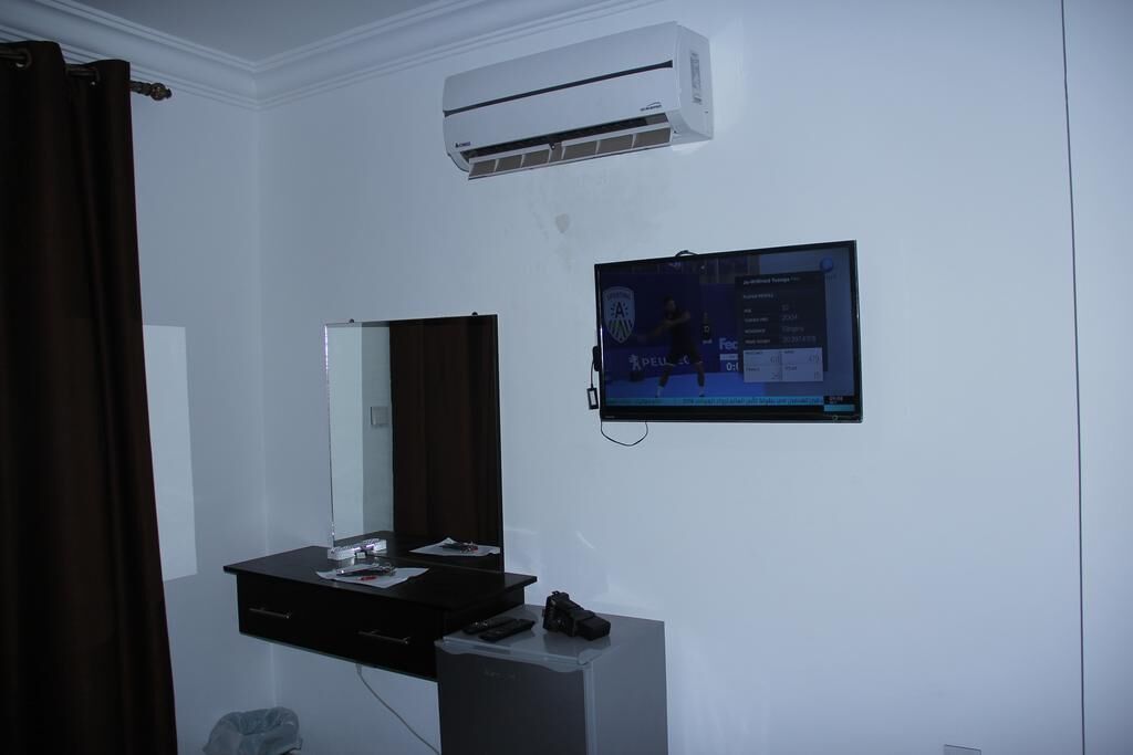 A hotel room with a black vanity, a mirror, a flat-screen TV mounted on the wall, and an air conditioning unit above the mirror.