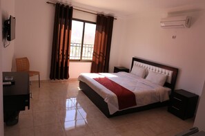 Une chambre à coucher comprenant un lit, un bureau, une chaise, une fenêtre avec des rideaux et un appareil de climatisation.
