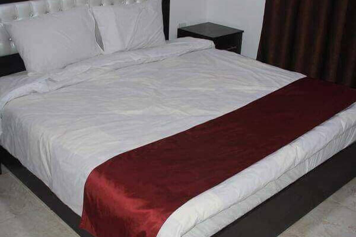 A neatly made bed with white linens and a red throw blanket, a dark wooden headboard, and a small bedside table.