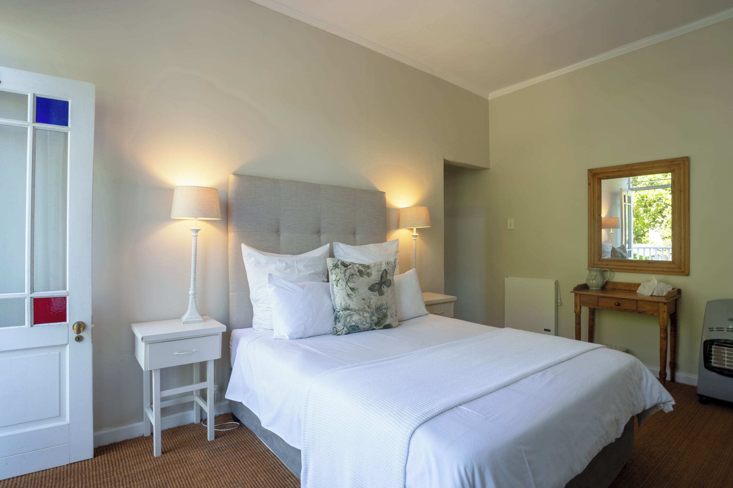 A bedroom with a bed, bedside lamps, a nightstand, a wooden table, and a mirror.