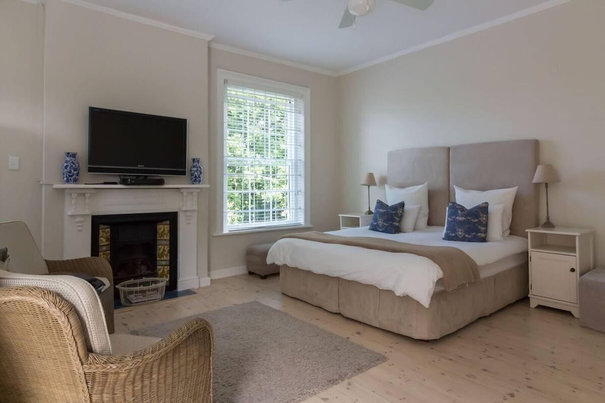 A bedroom with a bed, a television, a fireplace, and a window with blinds.
