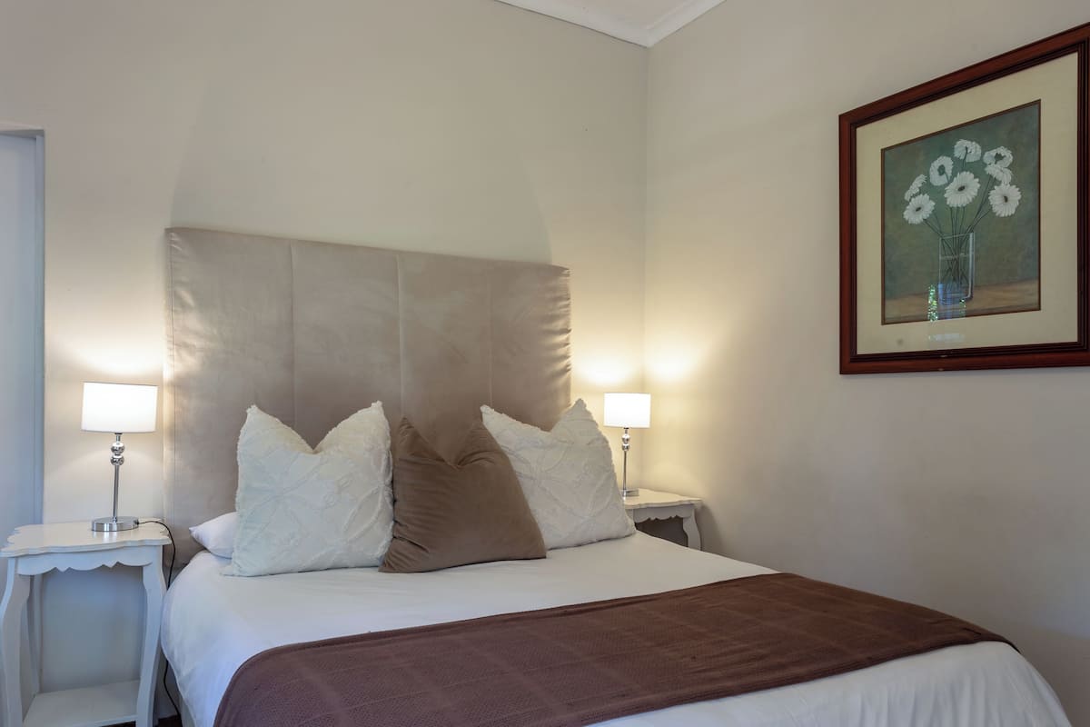 A neatly made bed with a brown blanket, two bedside tables with lamps, and a framed picture on the wall.