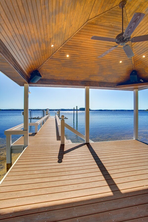 A wooden deck with a ceiling fan, overlooking a calm body of water.